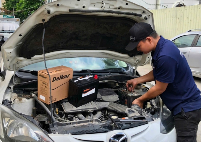 Kỹ thuật viên thay bình ắc quy Delkor cho xe ô tô Mazda tại gara